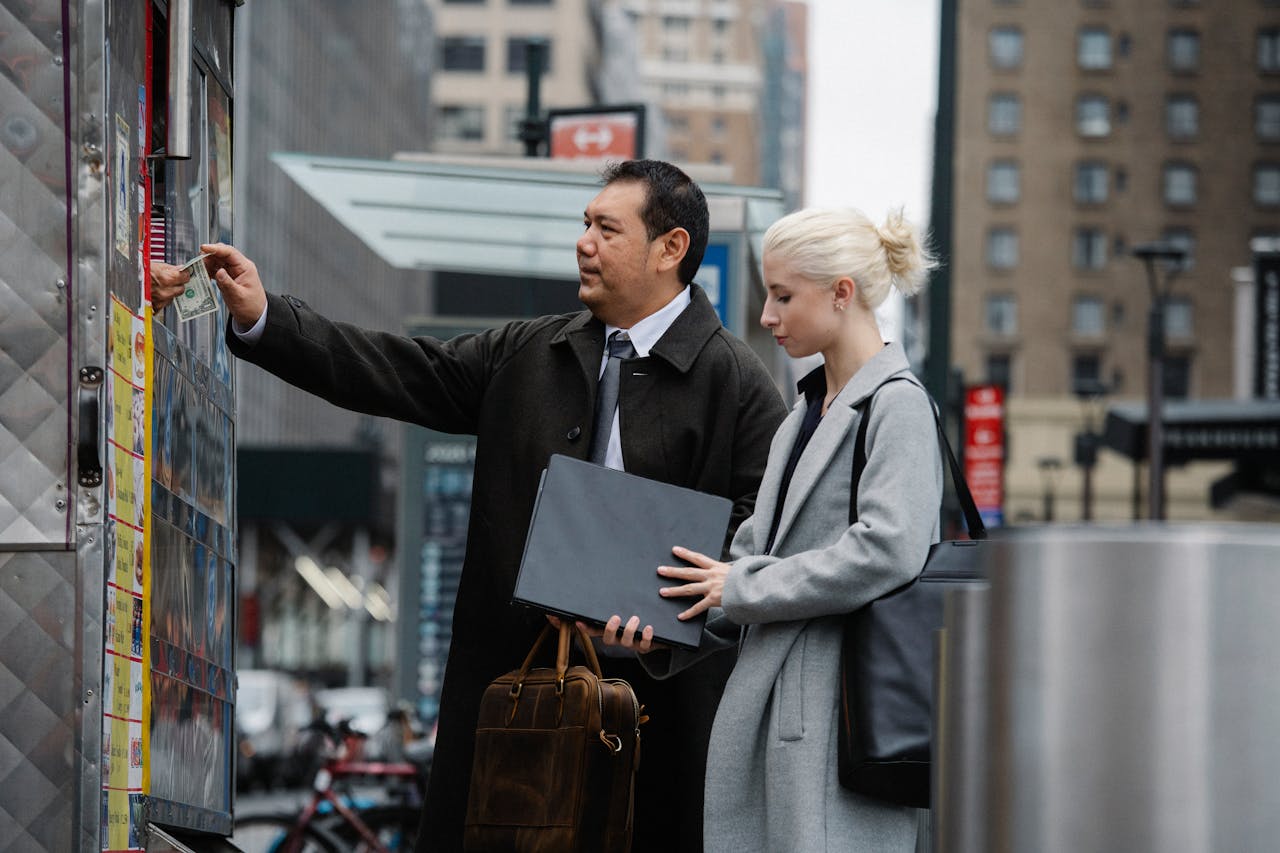 Side view of middle aged ethnic businessman paying for purchases while standing with young female colleague on street during break