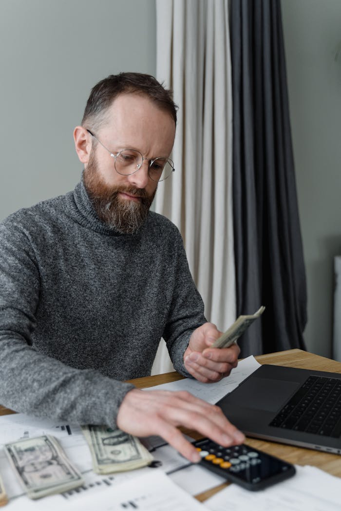 Man in Gray Sweater Computing Money